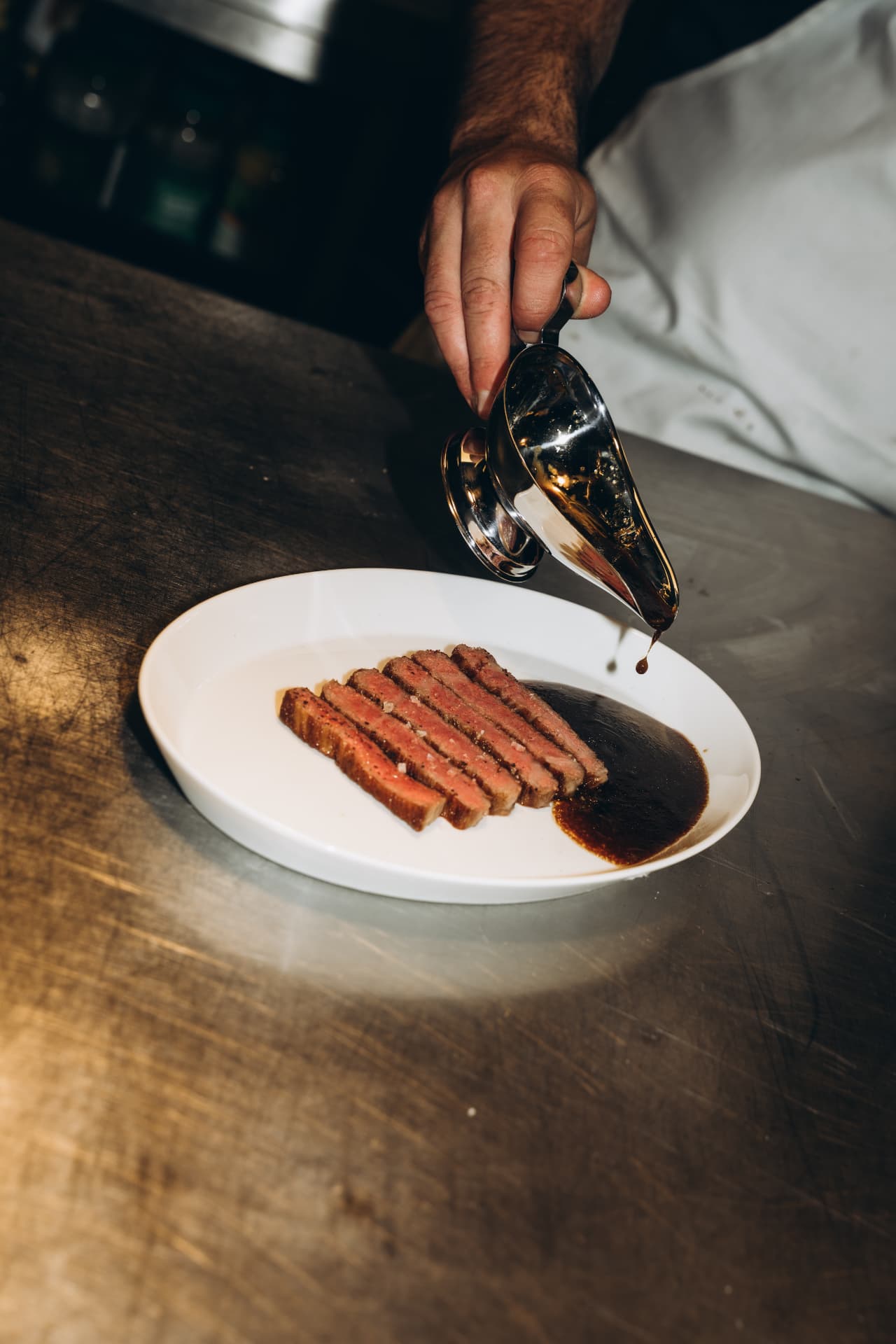 Gesneden wagyu steak waar jus overheen wordt geschonken in de keuken