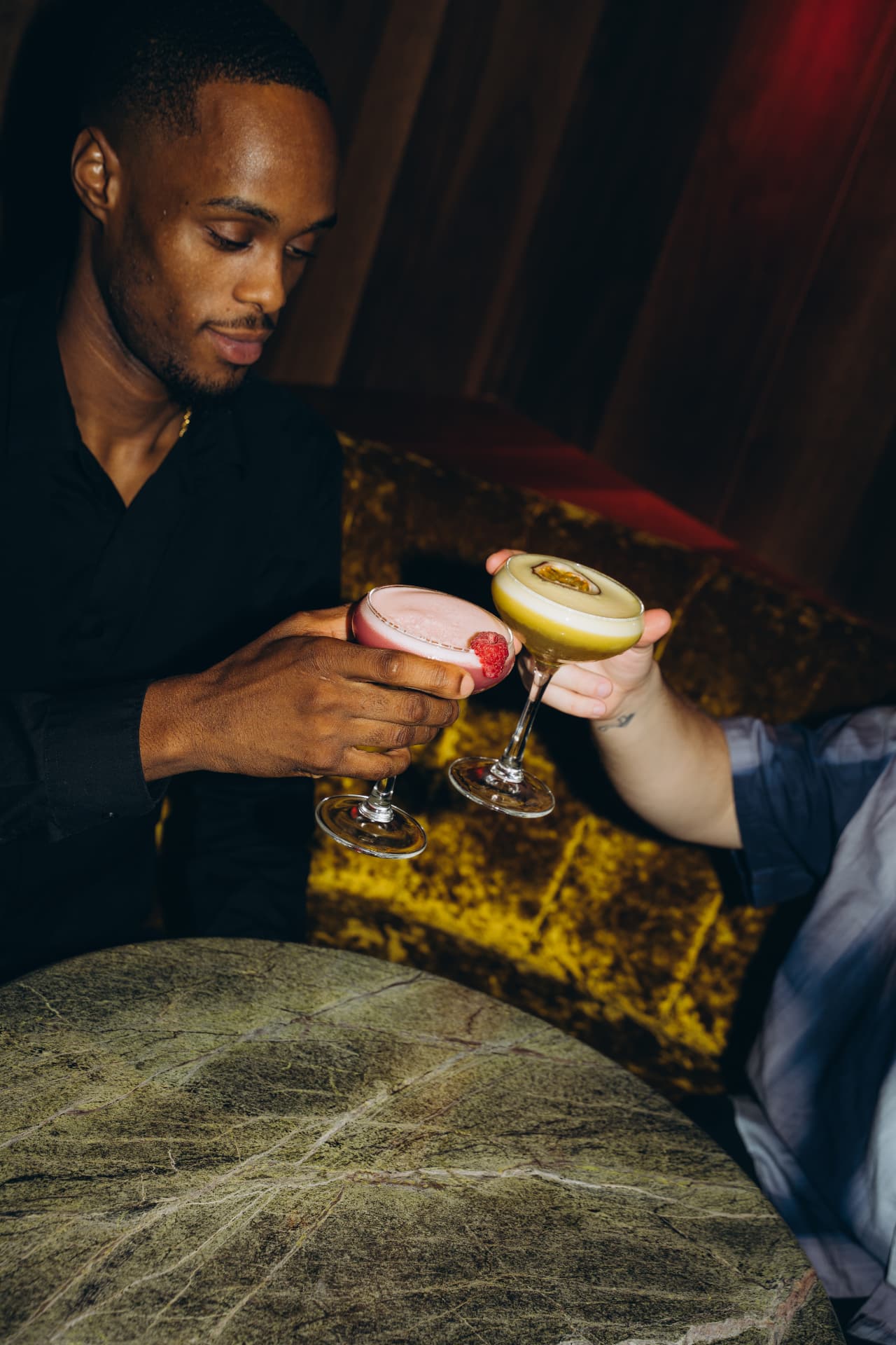 Twee gasten toosten met cocktails in een fluwelen booth